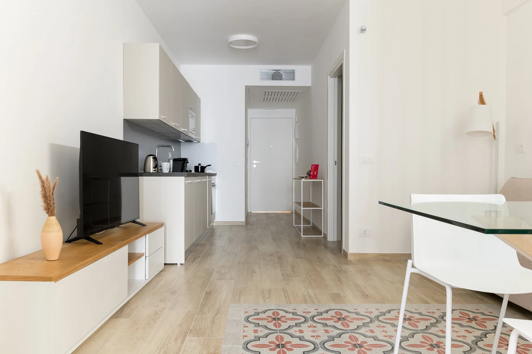 A bright studio room with a kitchenette, dining table, and television.