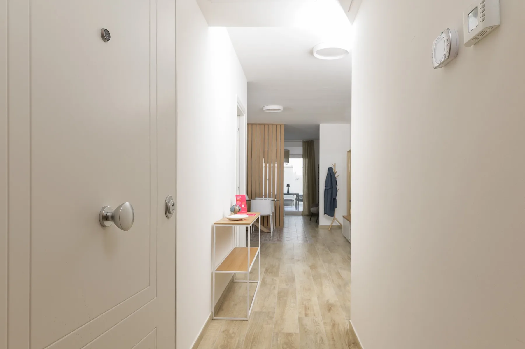 A bright hallway with a narrow console table and a coat hanging near the far end.