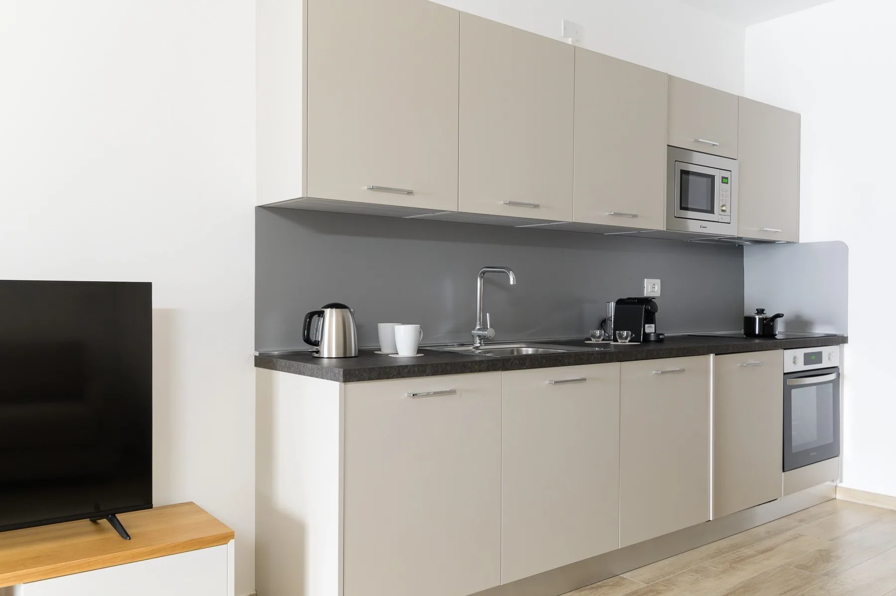 A modern kitchen with beige cabinets, a countertop, and a television at the side.