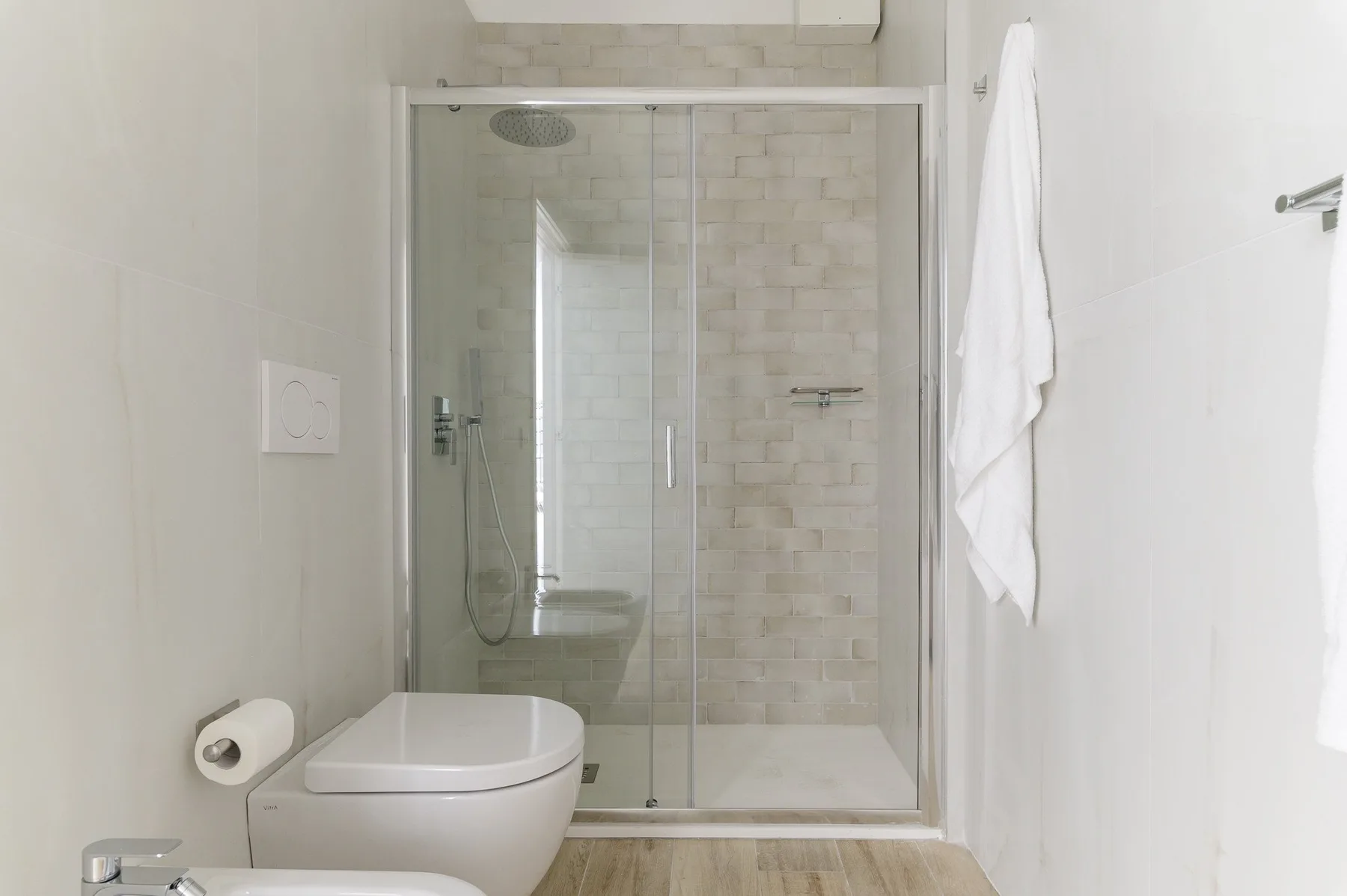 A bright bathroom with a glass shower and a toilet.