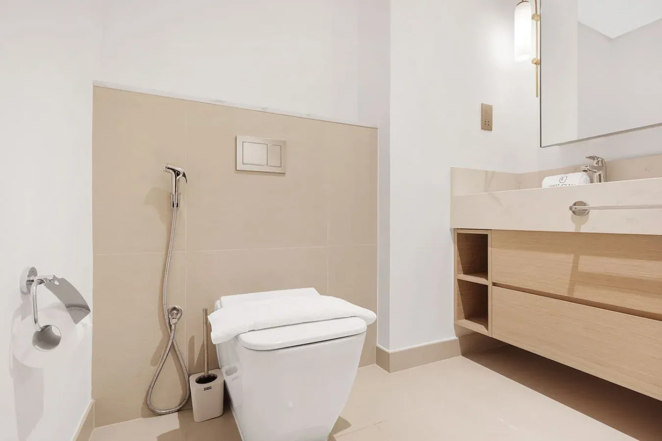 A bathroom with a toilet, handheld shower, and wood-toned vanity.