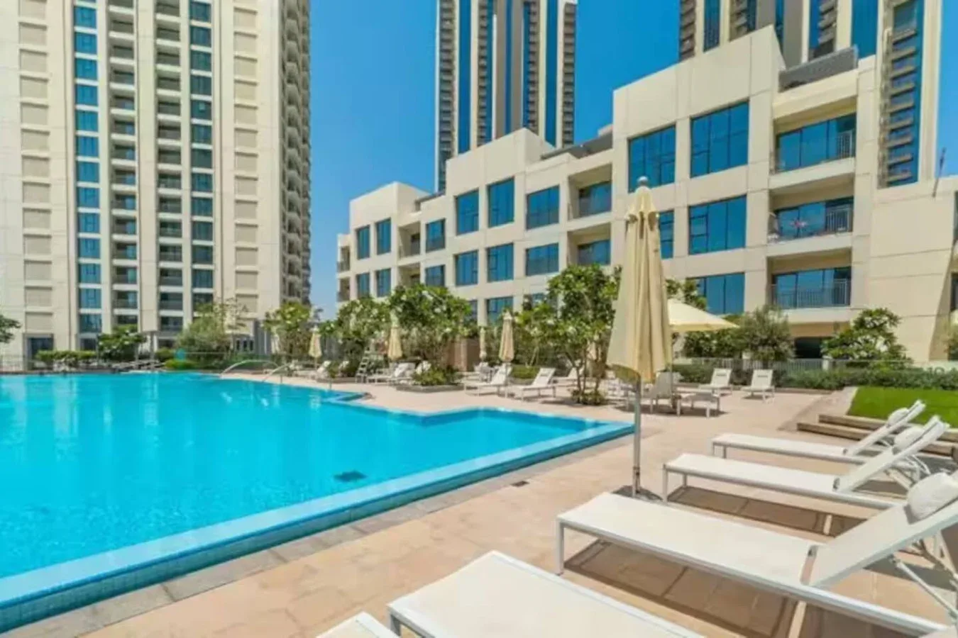 An outdoor swimming pool is surrounded by lounge seating and tall buildings.