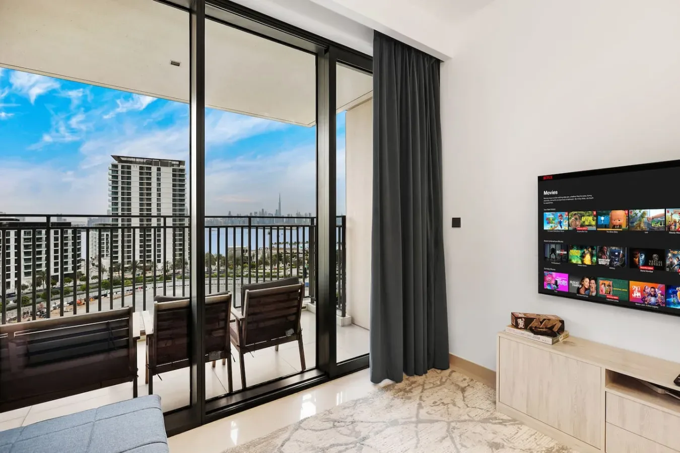 A bright living area opens onto a balcony with seating and a city view.