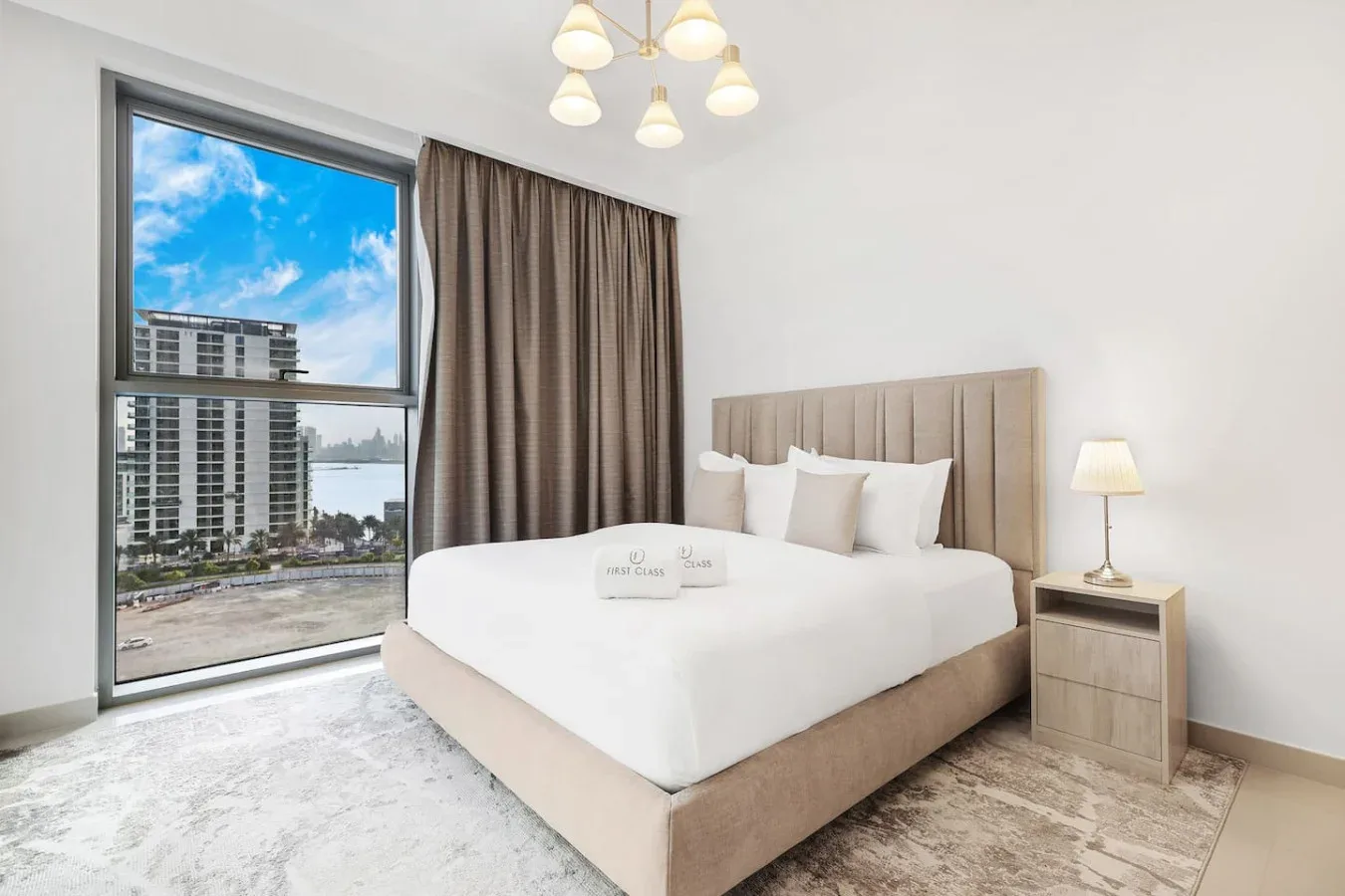 A bedroom with a large bed beside a window overlooking nearby buildings.