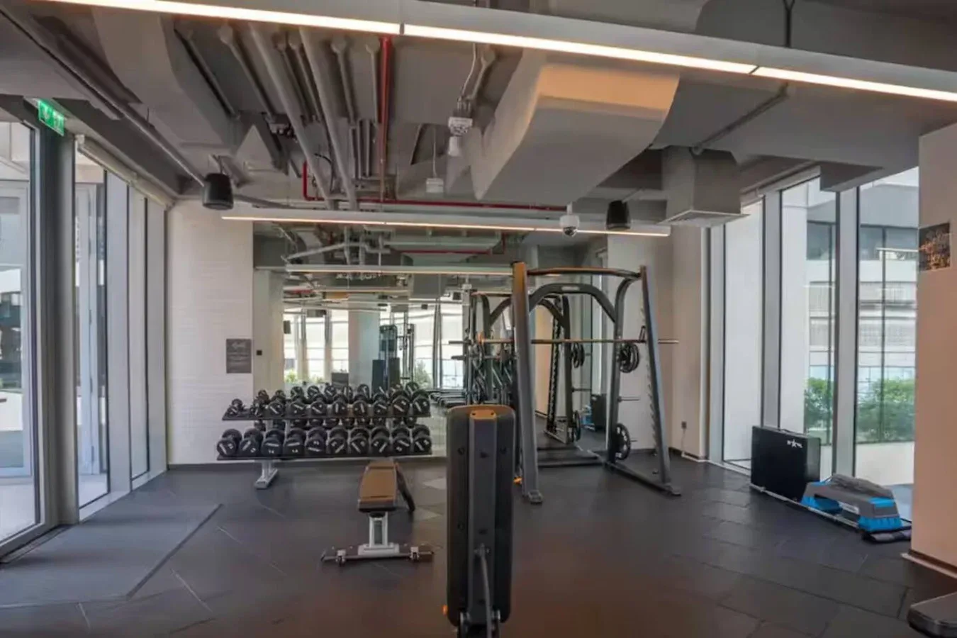 A gym with weight racks and exercise equipment beside large windows.