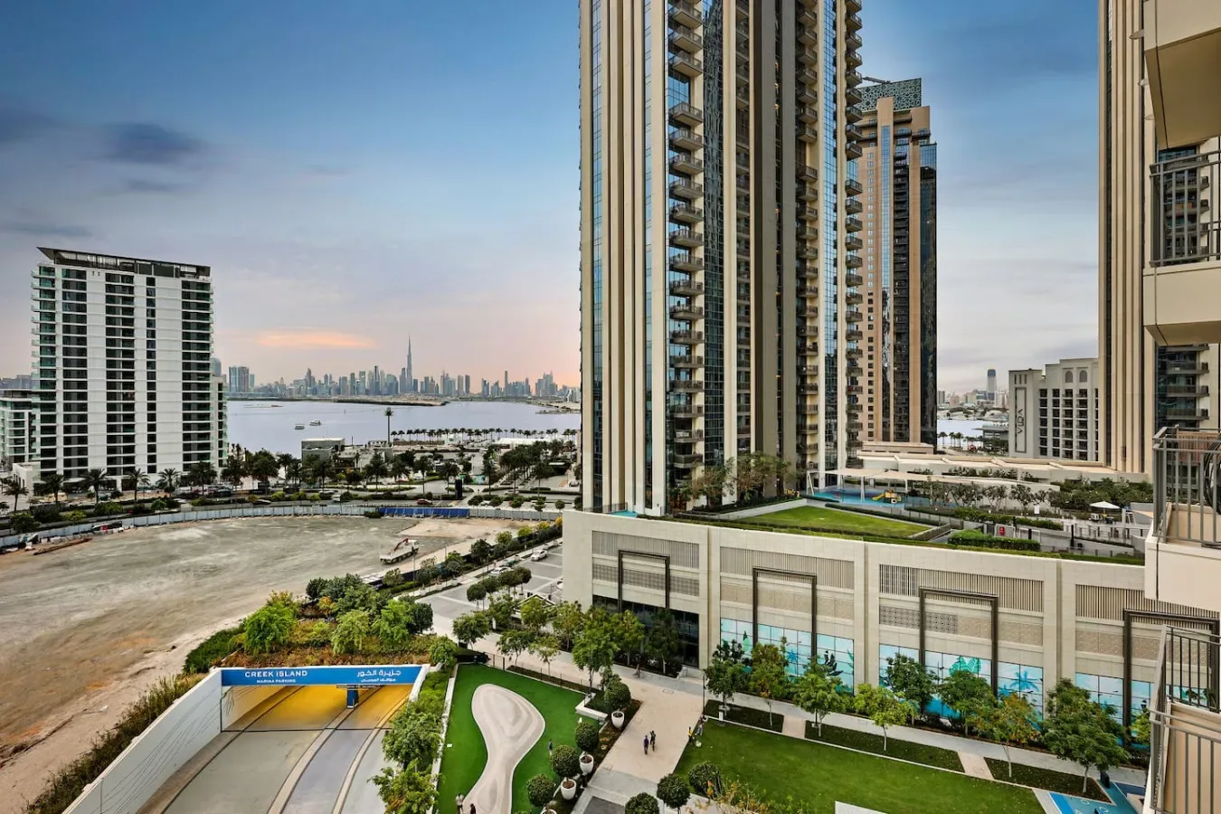 High-rise buildings overlook a waterfront skyline, with landscaped grounds and a pool in the foreground.