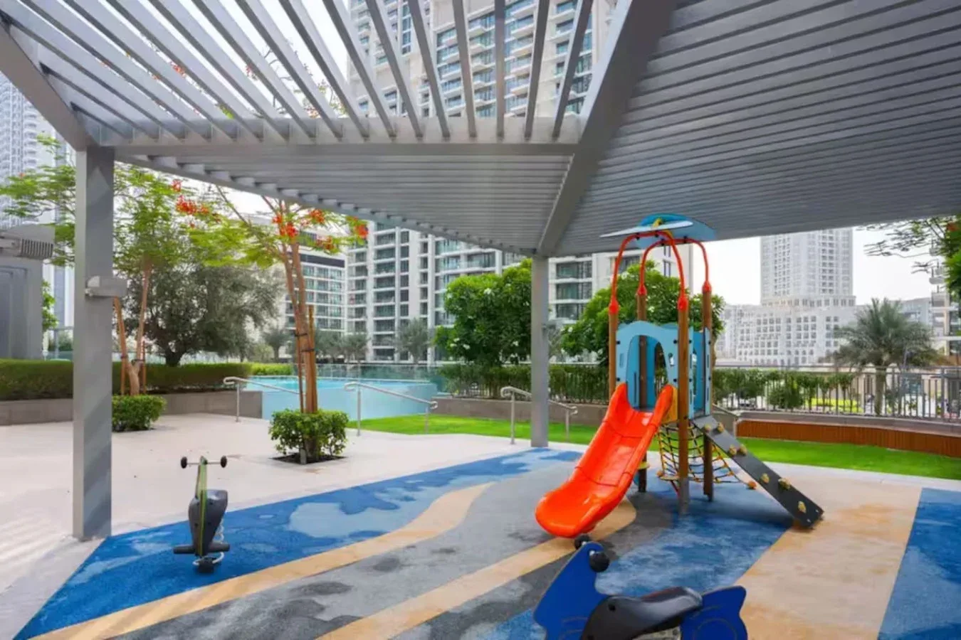 A covered outdoor playground has a colorful slide beside a swimming pool.