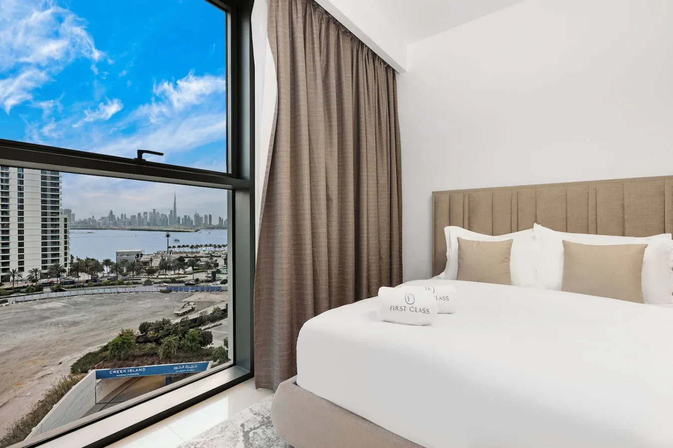 A bedroom with a large window overlooking water and nearby buildings.
