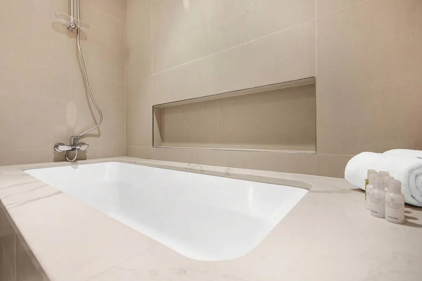 A tiled bathroom with a bathtub, wall-mounted shower, and toiletries.