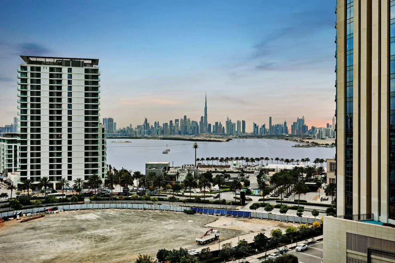 A city skyline rises across a body of water, framed by nearby buildings.