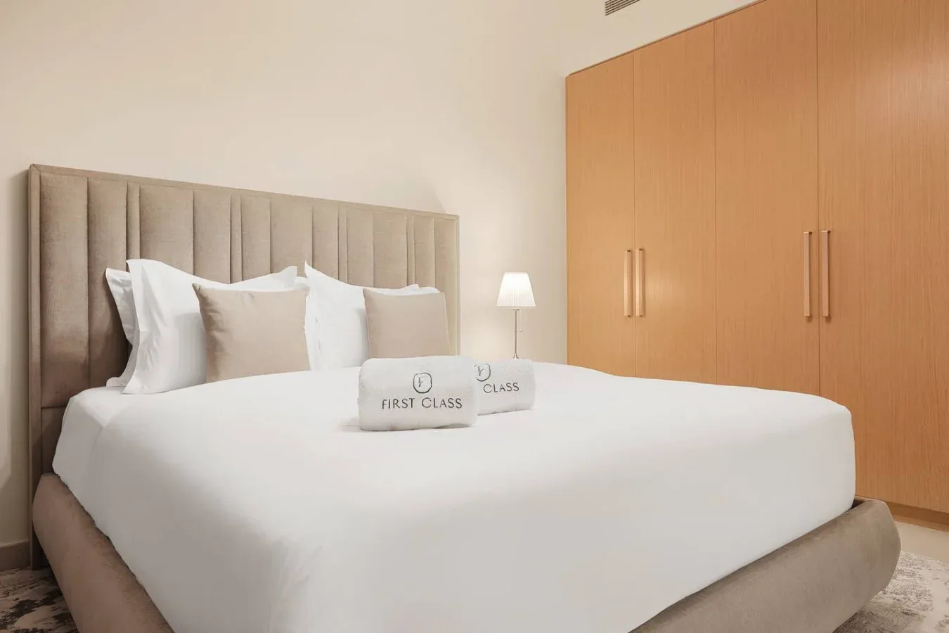 A bedroom with a neatly made bed, upholstered headboard, and wooden wardrobe.