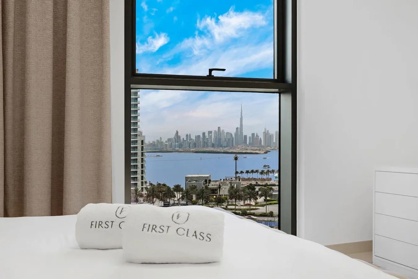 A bedroom with a large window overlooking the water and distant city skyline.