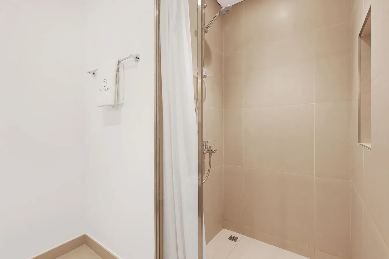 A tiled bathroom shower area with a wall-mounted showerhead and controls.