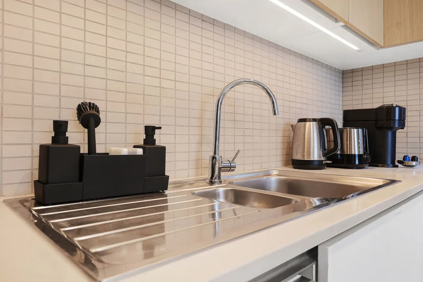 A tiled kitchen counter with a sink, faucet, and small appliances.