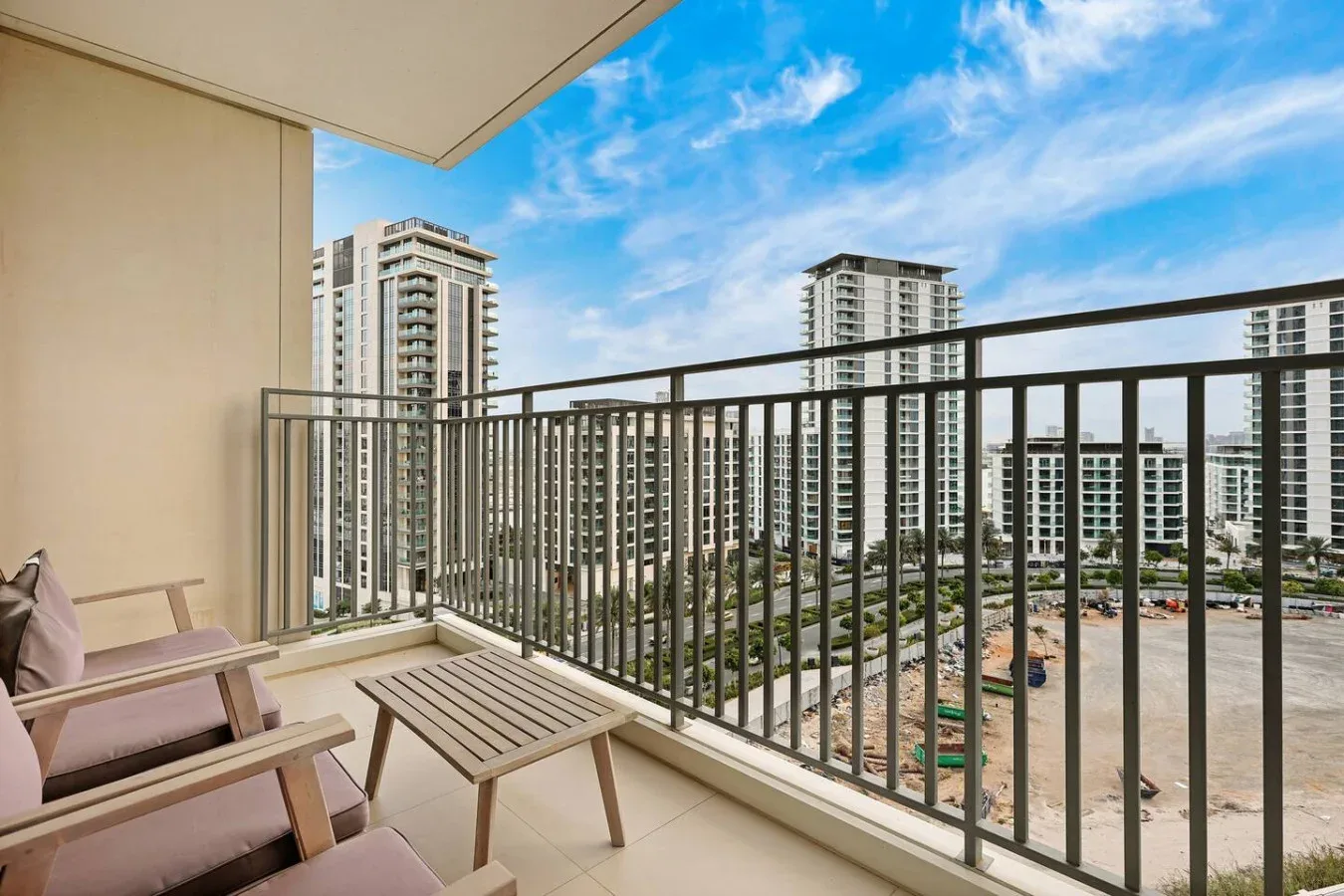 A balcony with seating overlooks nearby high-rise buildings and a construction site.