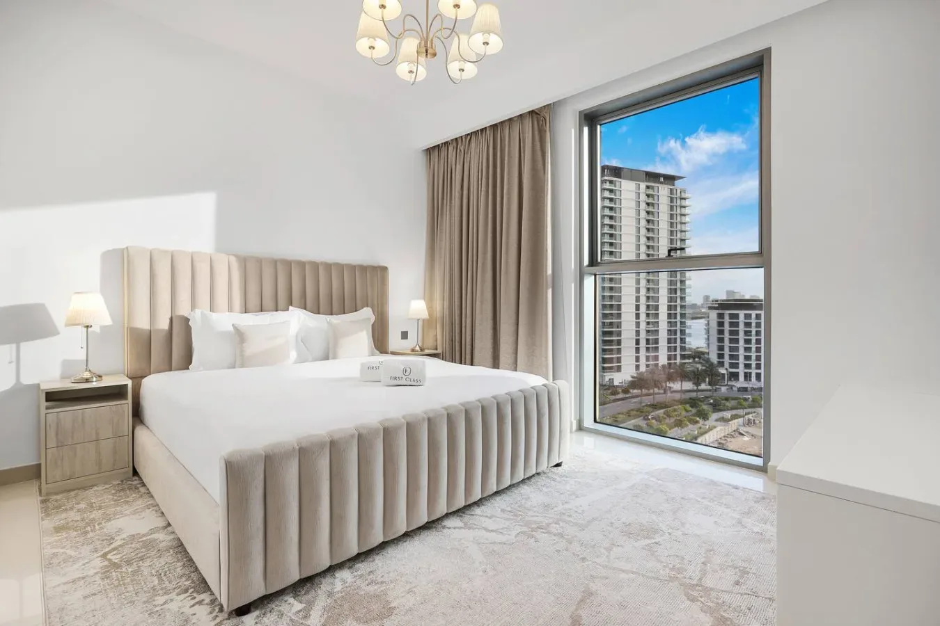 A bright bedroom with a large upholstered bed beside a floor-to-ceiling window.