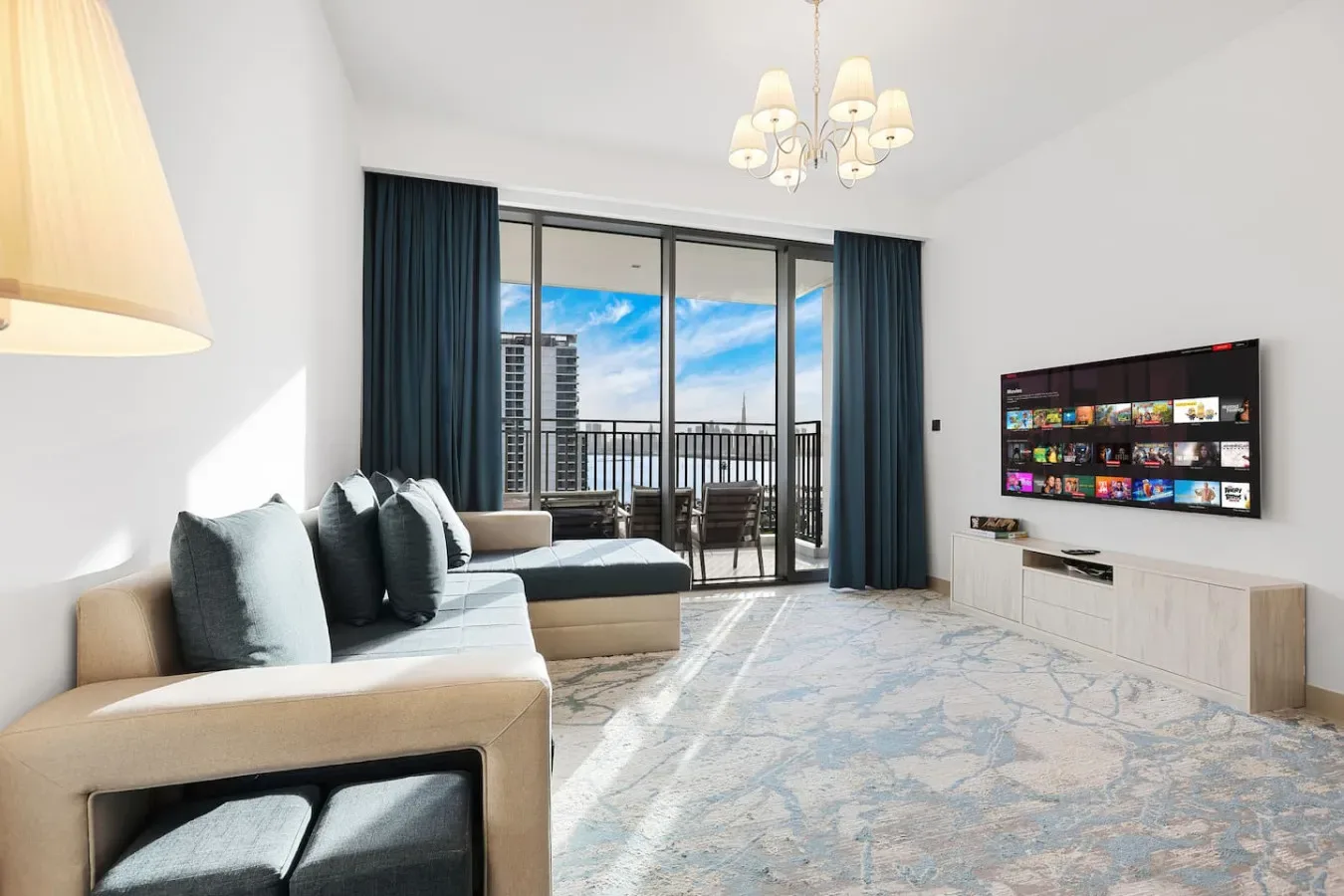 A bright living room with seating, a television, and glass doors opening onto a balcony.