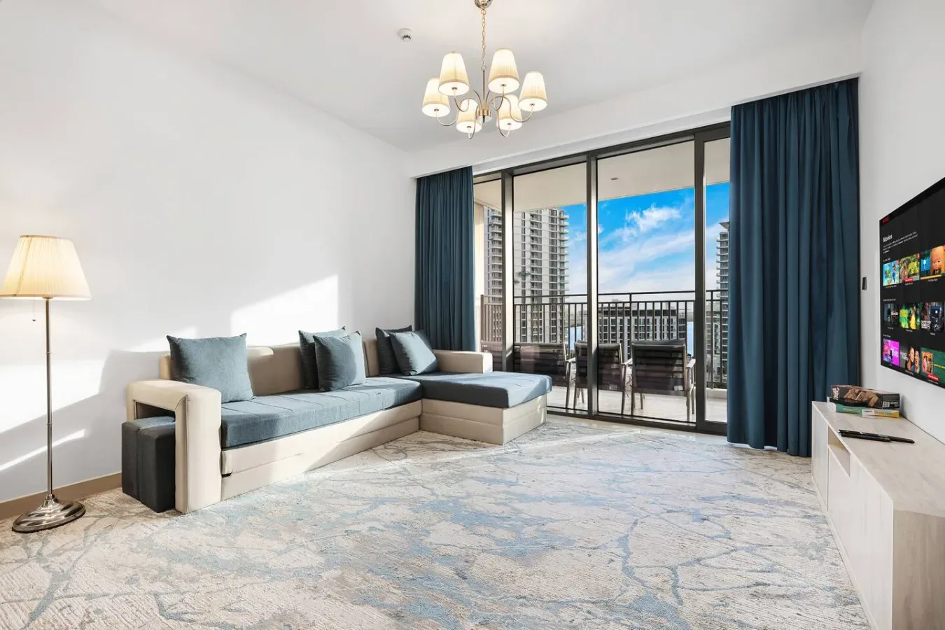 A bright living room with sectional seating and large windows opening onto a balcony.
