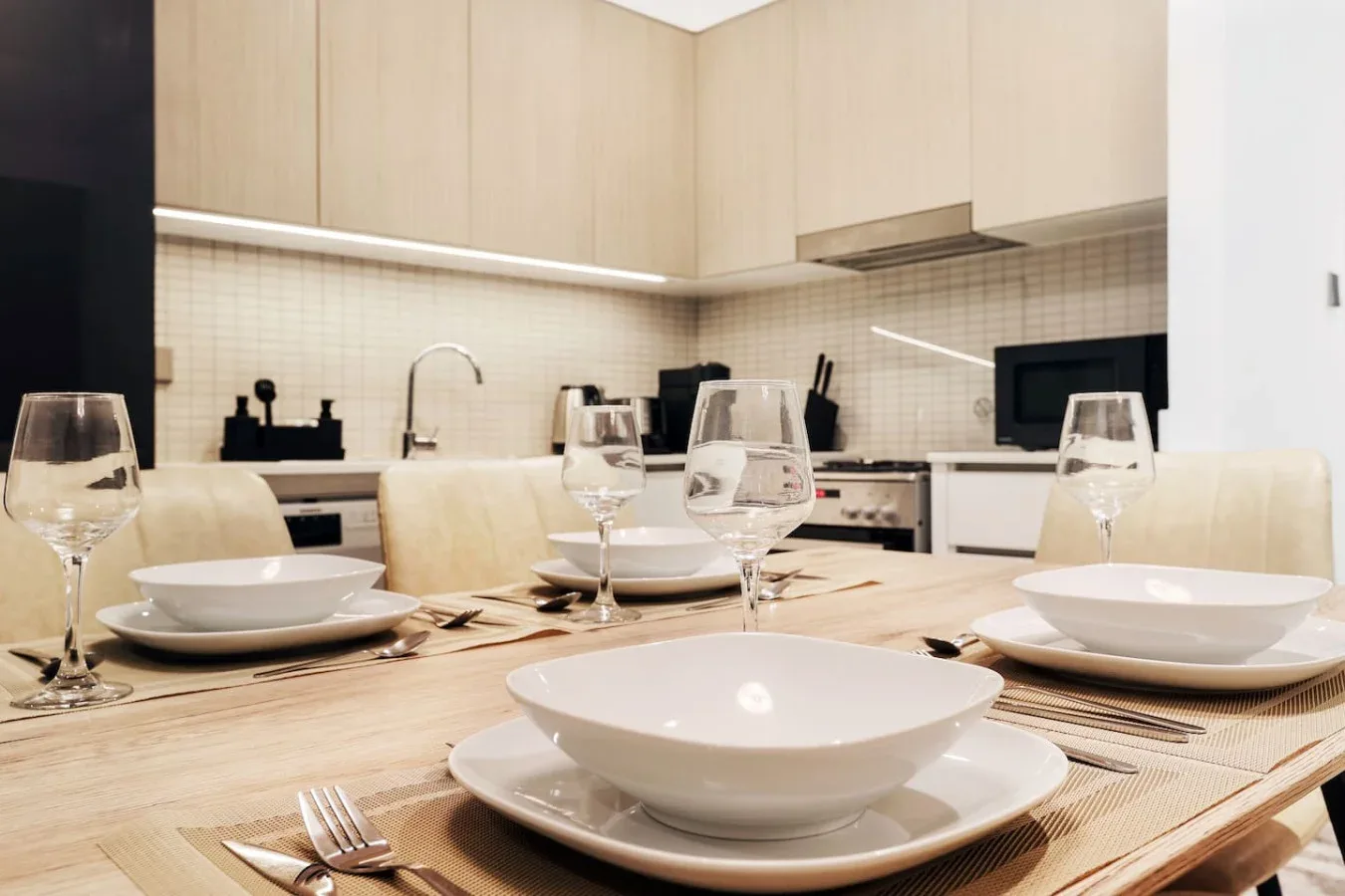 A dining table is set with dishes and glasses in a bright kitchen.