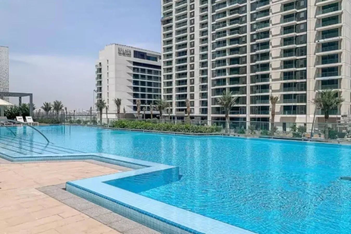 An outdoor swimming pool sits beside paved decking and tall modern buildings.
