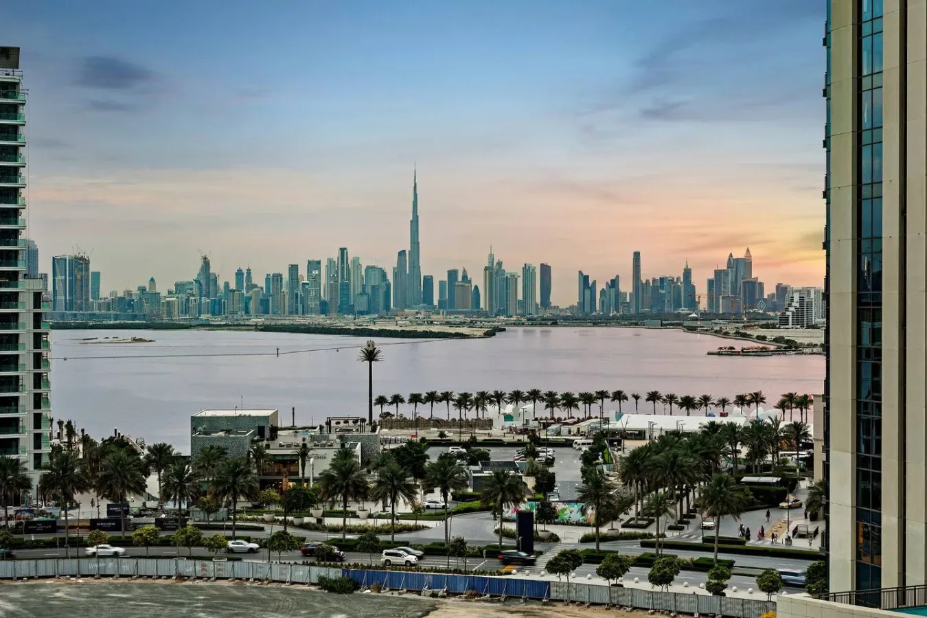 A city skyline rises beyond a waterfront, with palm-lined streets in the foreground.