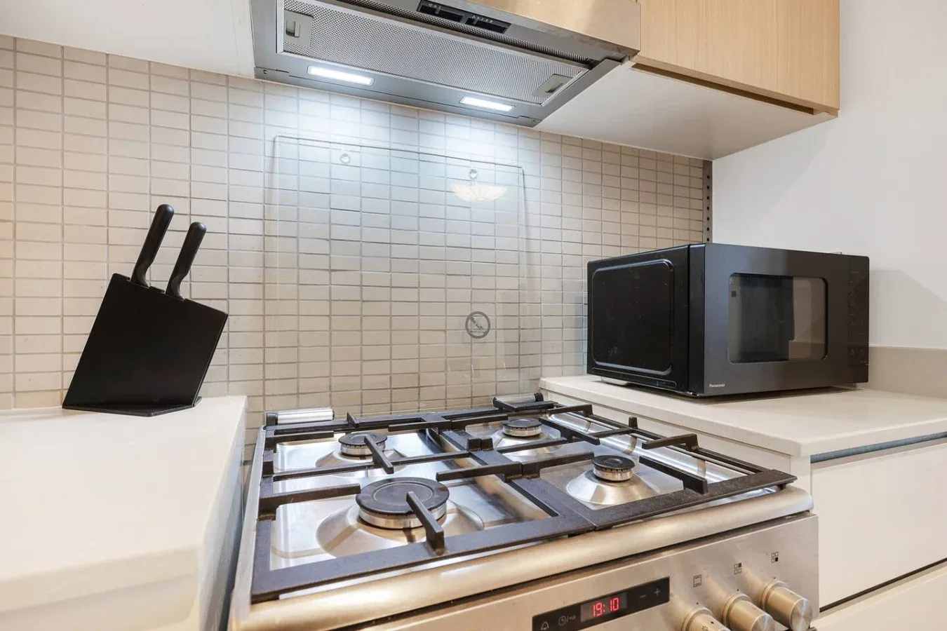 A kitchen with a stainless-steel gas cooktop, range hood, and countertop microwave.