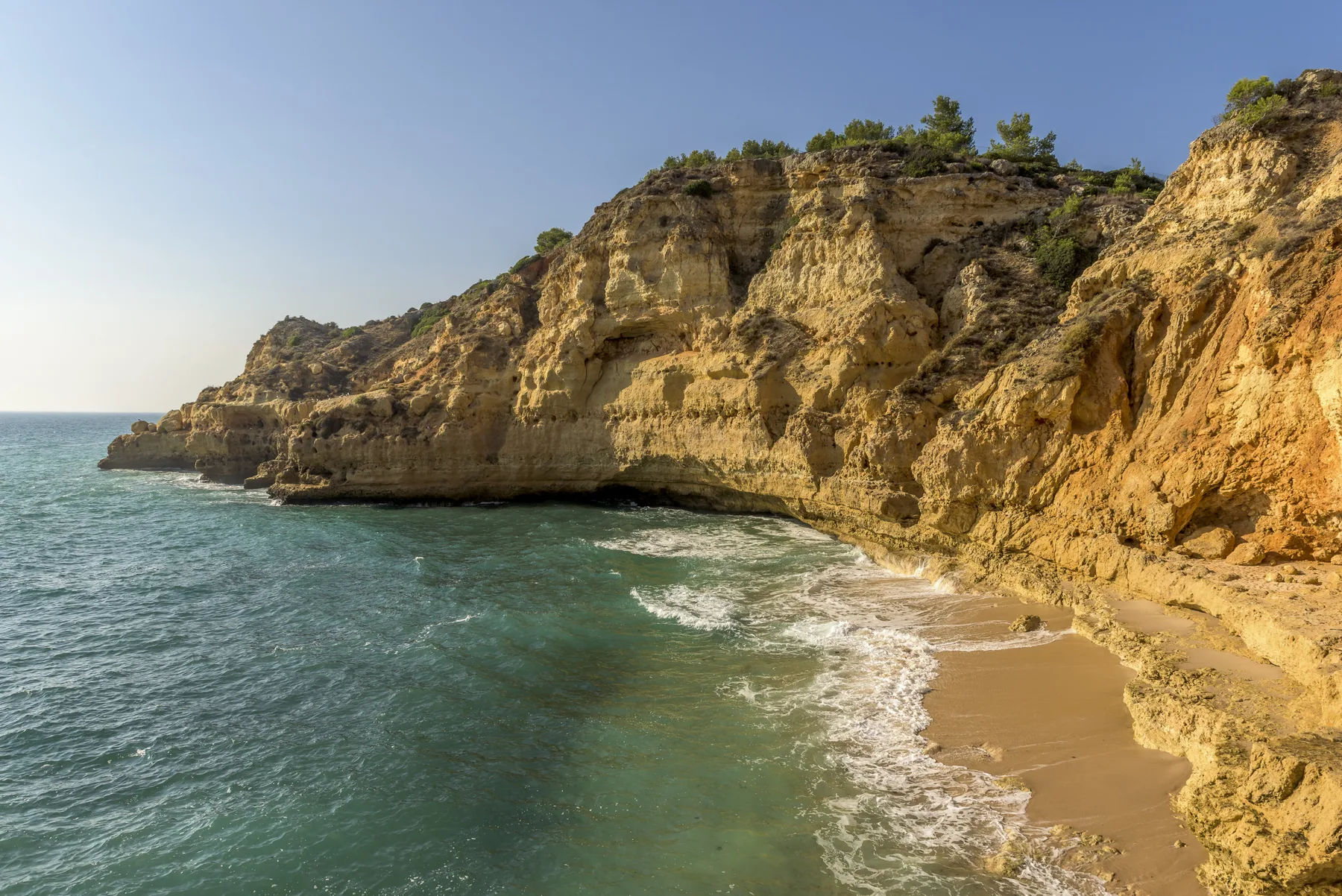Coastal beach with turquoise water beneath rocky cliffs.