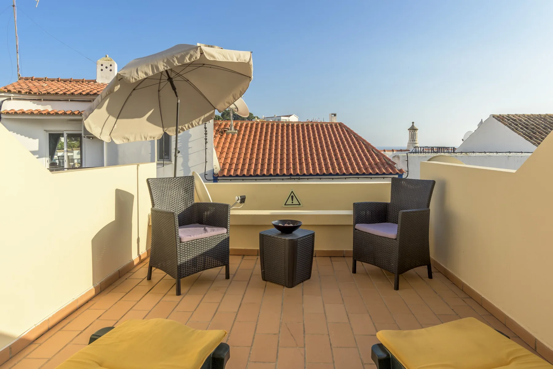 A tiled terrace has two armchairs, a small table, and a sun umbrella.