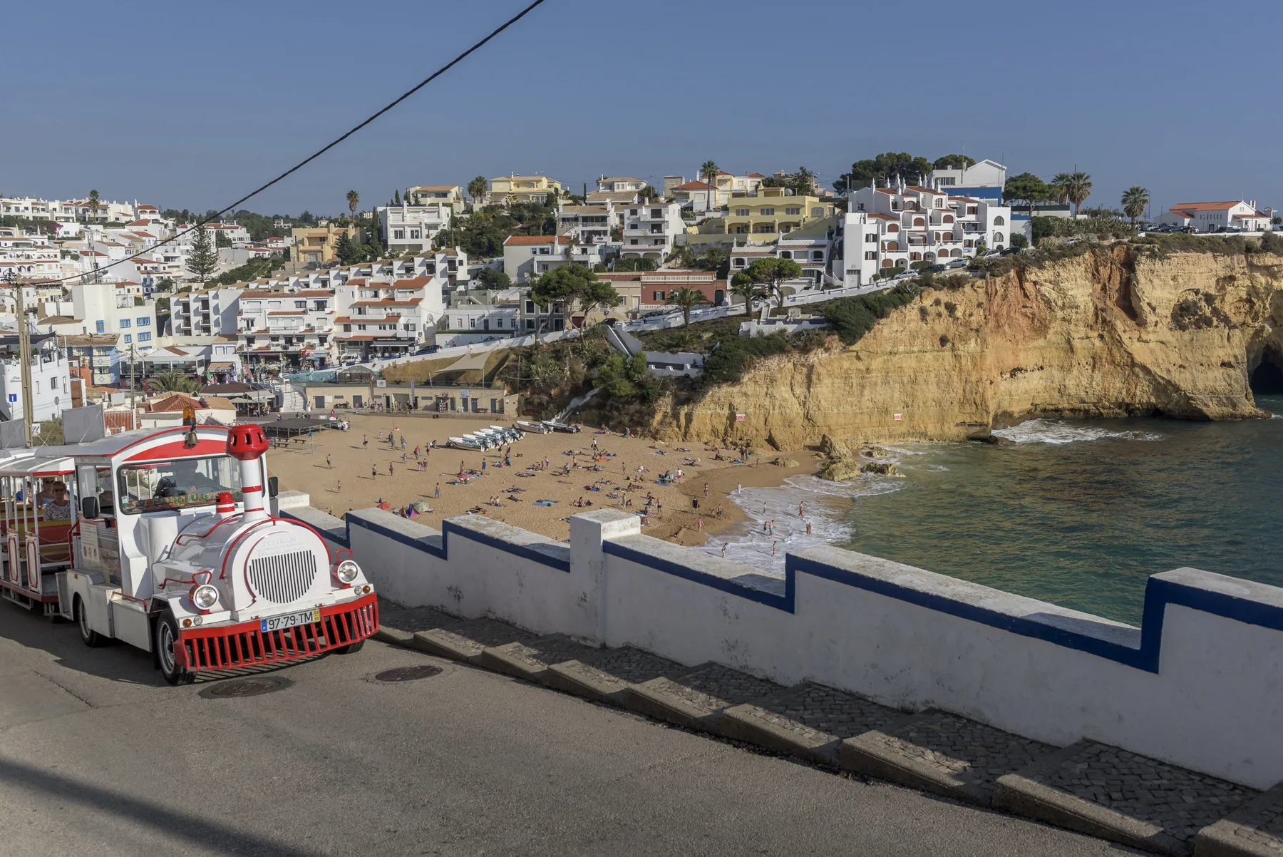 A coastal beach and cliffside town overlook the sea beside a road.