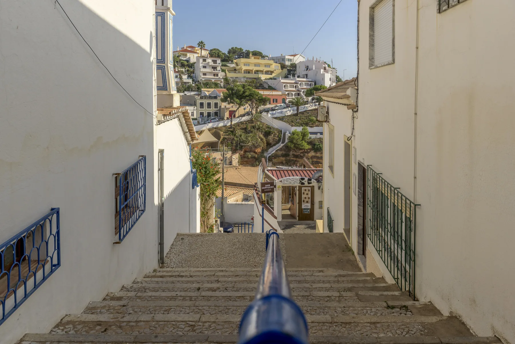 A stone stairway descends between white buildings toward a hillside neighborhood.