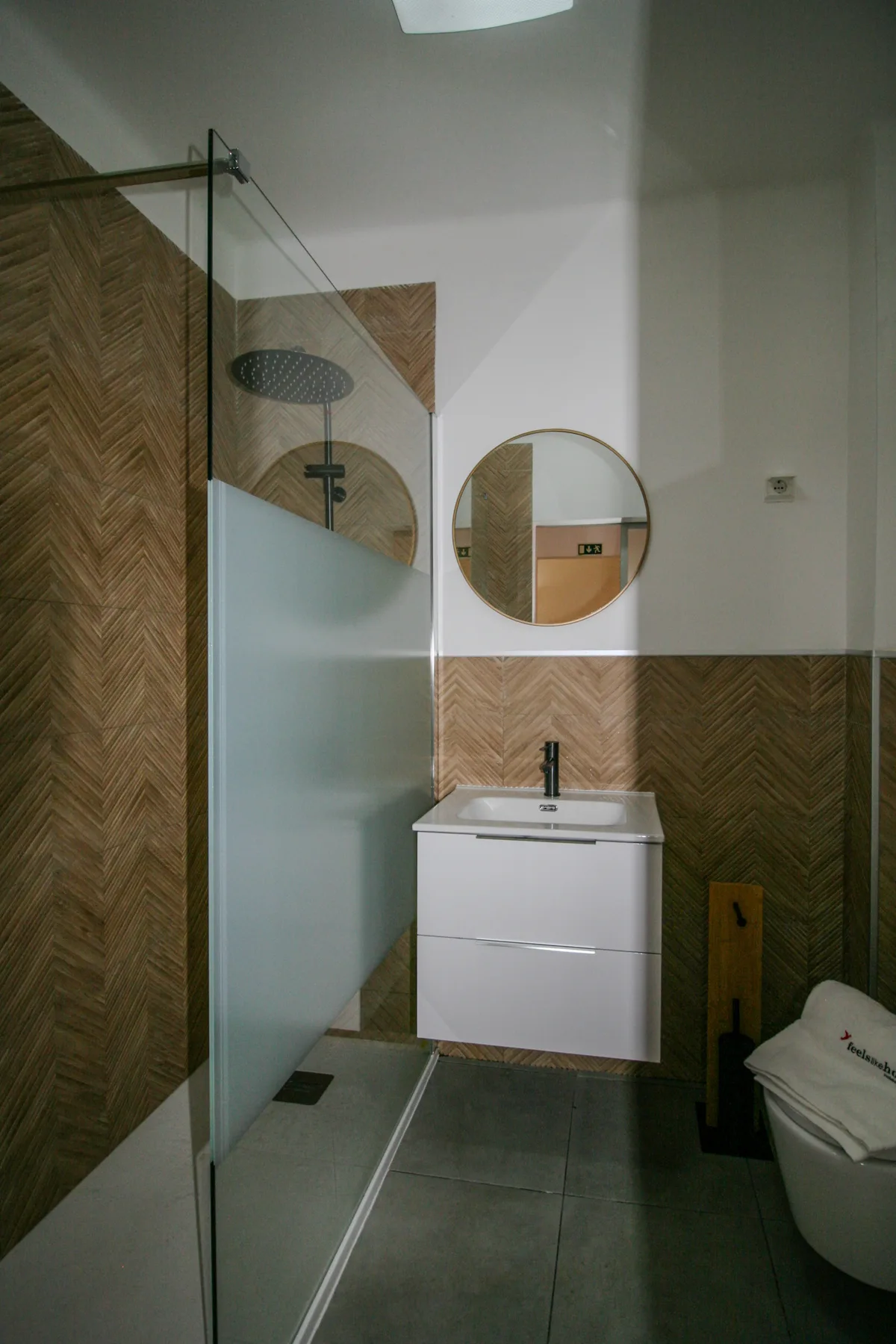 A bathroom with a glass shower, wall-mounted sink, and round mirror.