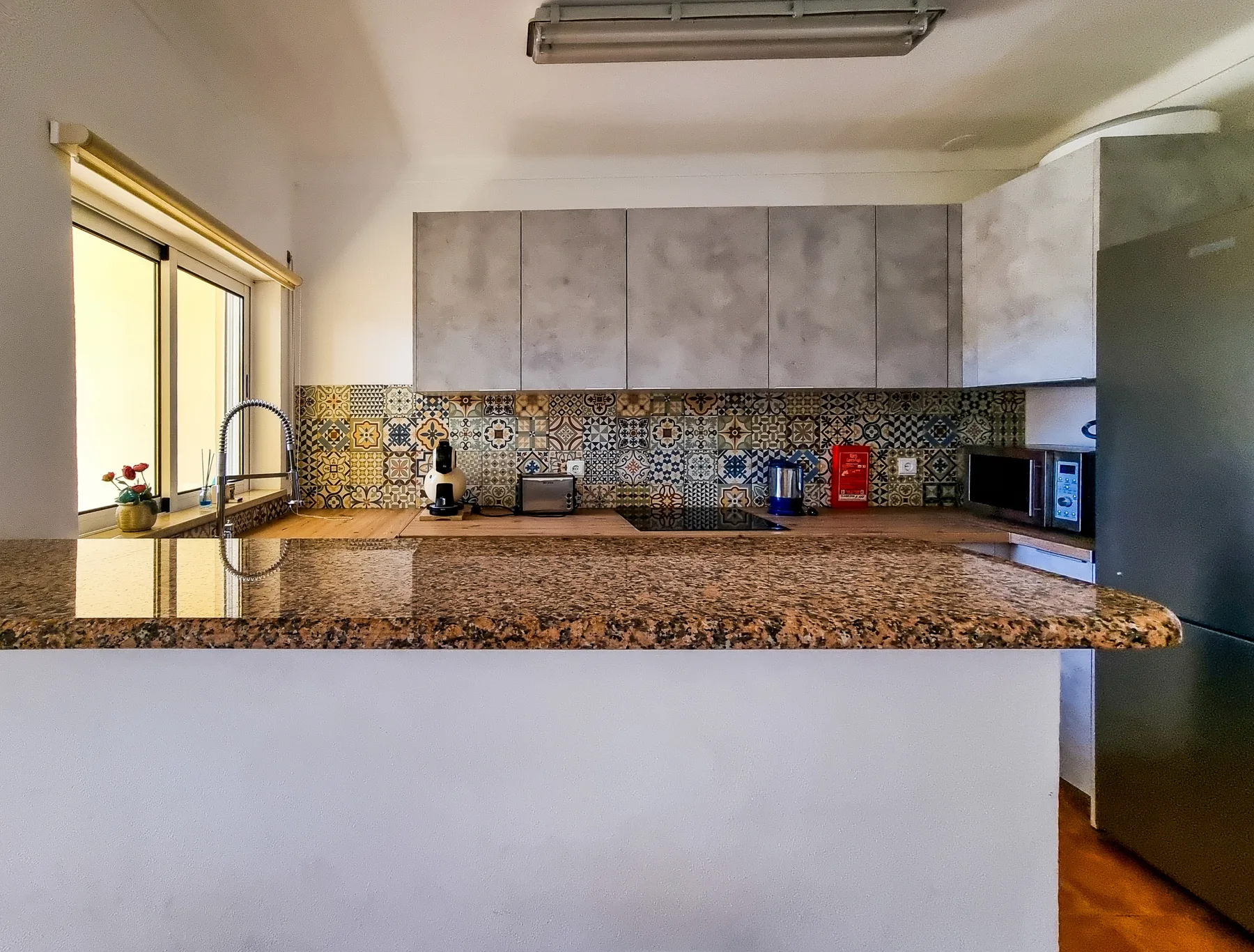 A kitchen with a wide counter, sink, and patterned backsplash.