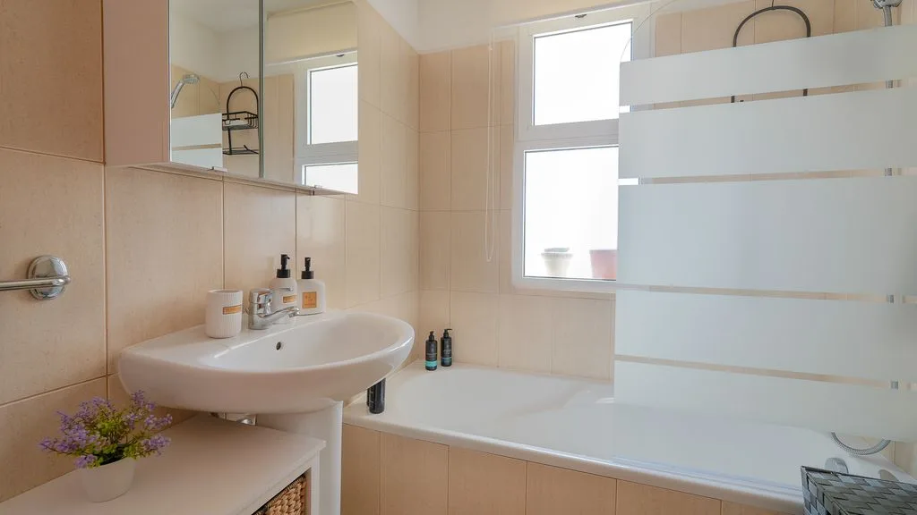 Un baño con bañera, lavabo y mampara de vidrio translúcido.