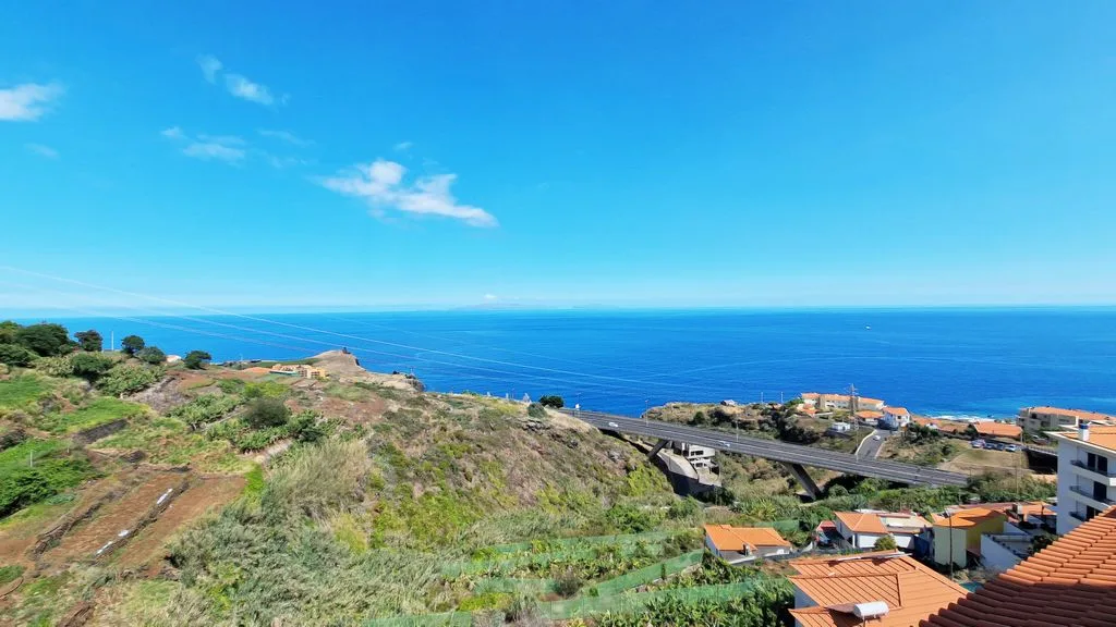 Paisaje costero con océano azul, vegetación en la ladera y edificios dispersos.