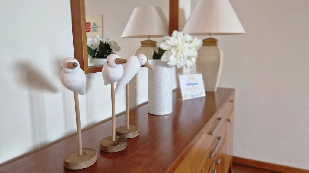 Una cómoda de madera exhibe esculturas decorativas de aves, flores y lámparas.