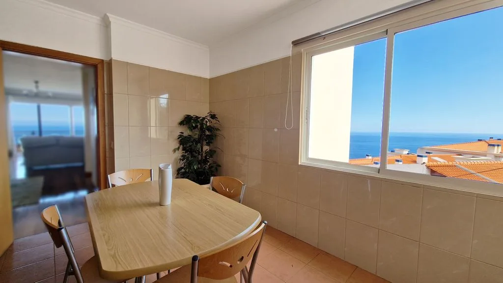 Comedor con una mesa y sillas junto a una ventana grande con vistas al mar.
