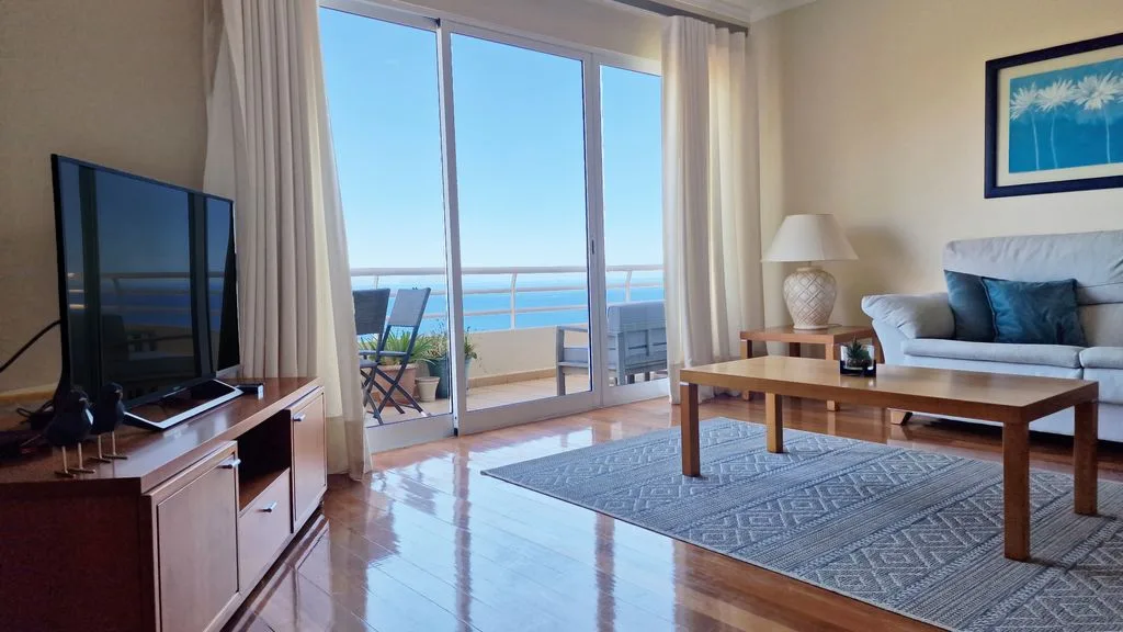 Una sala de estar con asientos y una mesa de centro junto a puertas de vidrio con vista al mar.