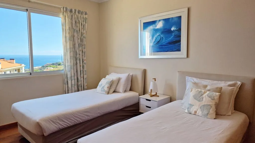 Un dormitorio con dos camas junto a una ventana con vistas al océano.