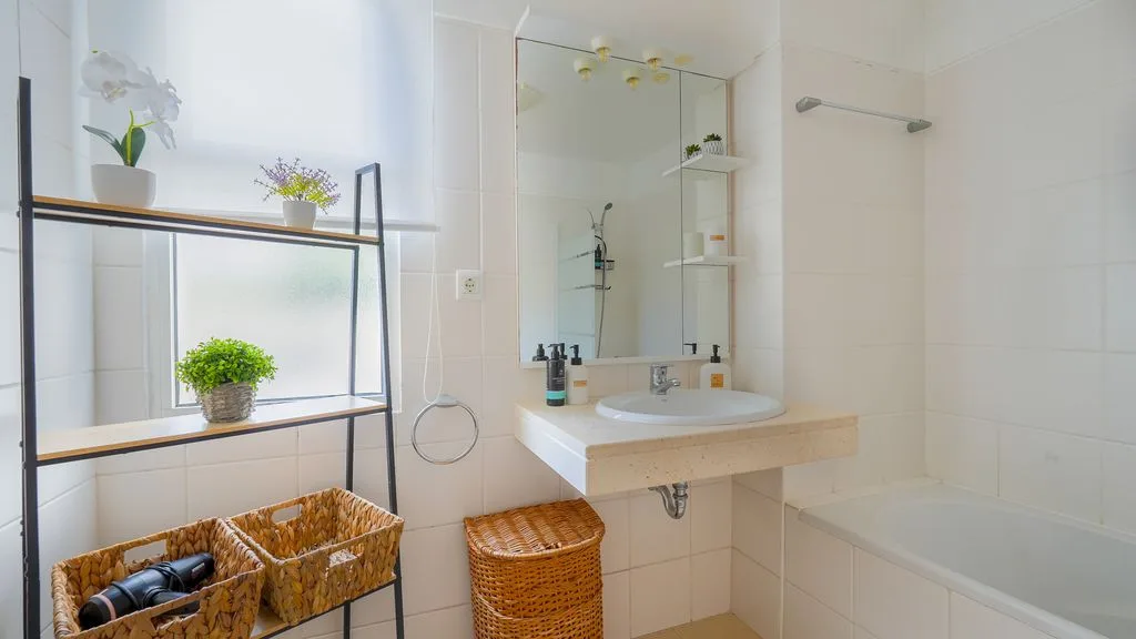 Un baño luminoso con lavabo, ducha y estanterías abiertas.