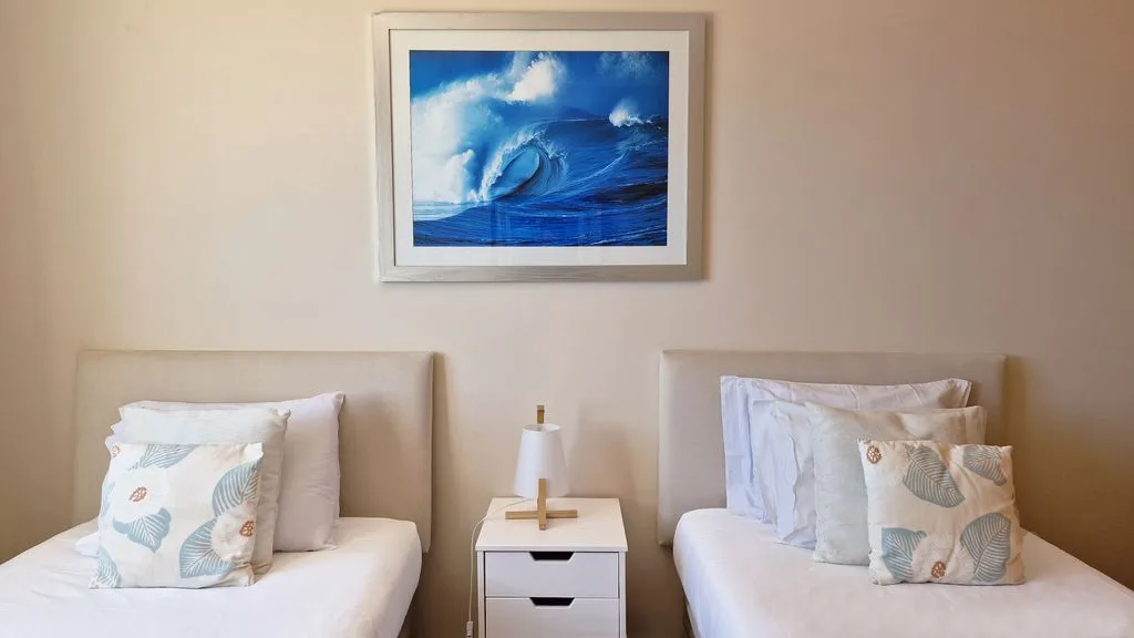 Un dormitorio con dos camas y una obra enmarcada del océano sobre ellas.