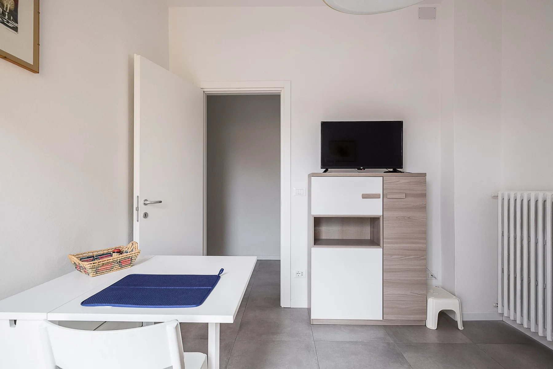 Una habitación luminosa con una mesa blanca, un televisor y una puerta abierta.