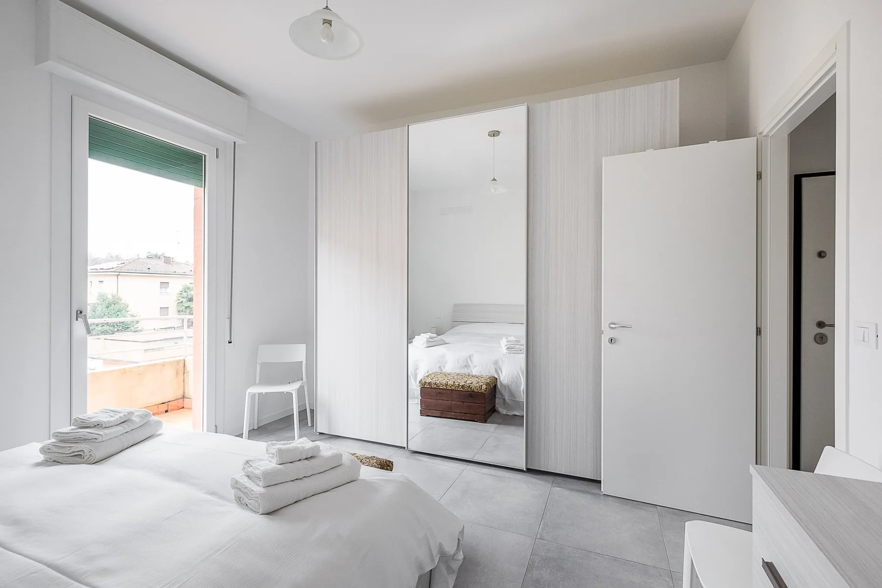 Un dormitorio luminoso con una cama, un armario con espejo y una puerta al balcón.