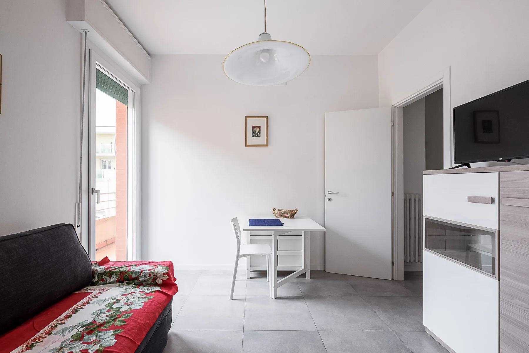 Una luminosa sala de estar con un escritorio pequeño y asientos junto a una puerta de balcón.