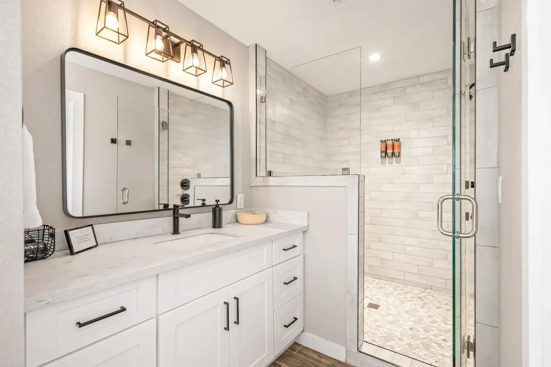 Baño moderno con una ducha con cerramiento de vidrio, un espejo grande sobre un mueble de baño con dos lavabos, armarios blancos y elegantes accesorios de iluminación.