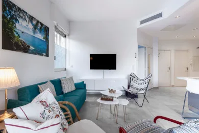A bright living room with a teal sofa, a television, and a small seating area.