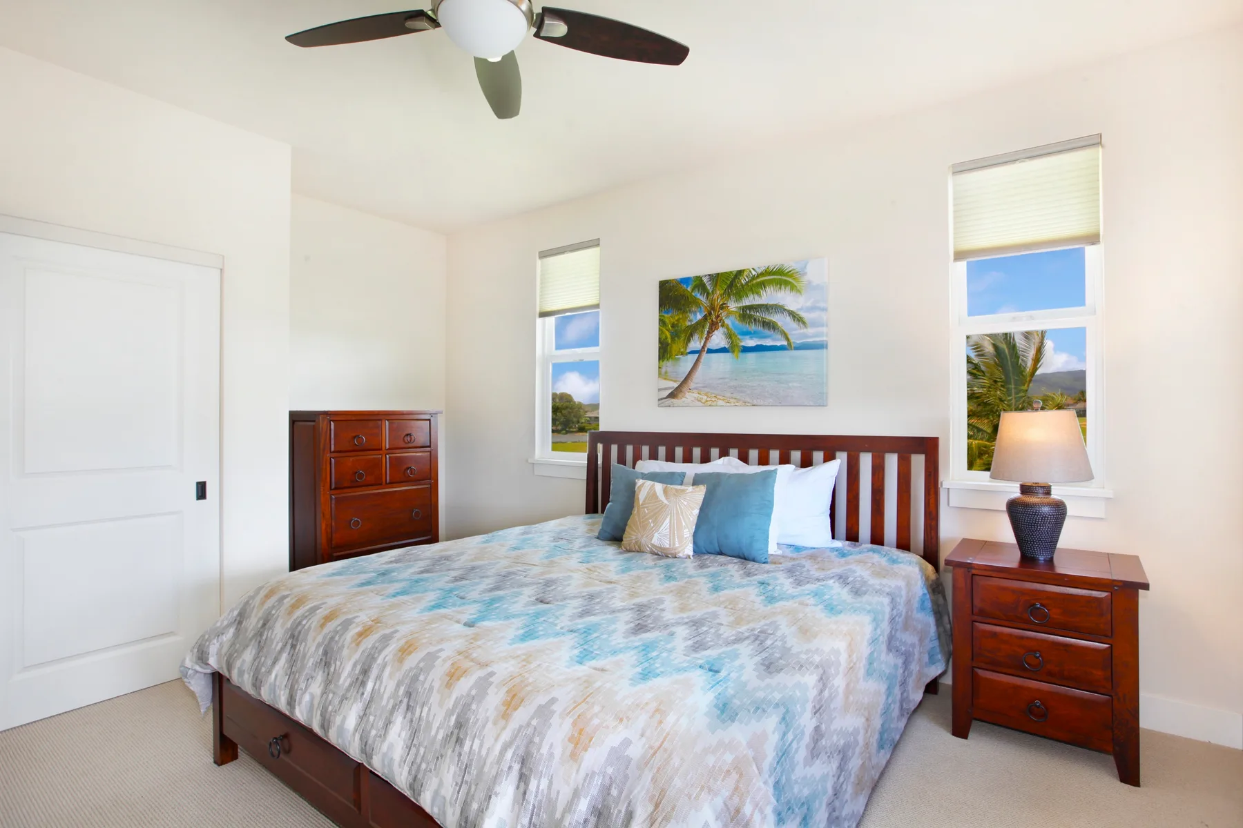 A bedroom with a wooden bed, patterned bedding, and a palm-tree wall picture.