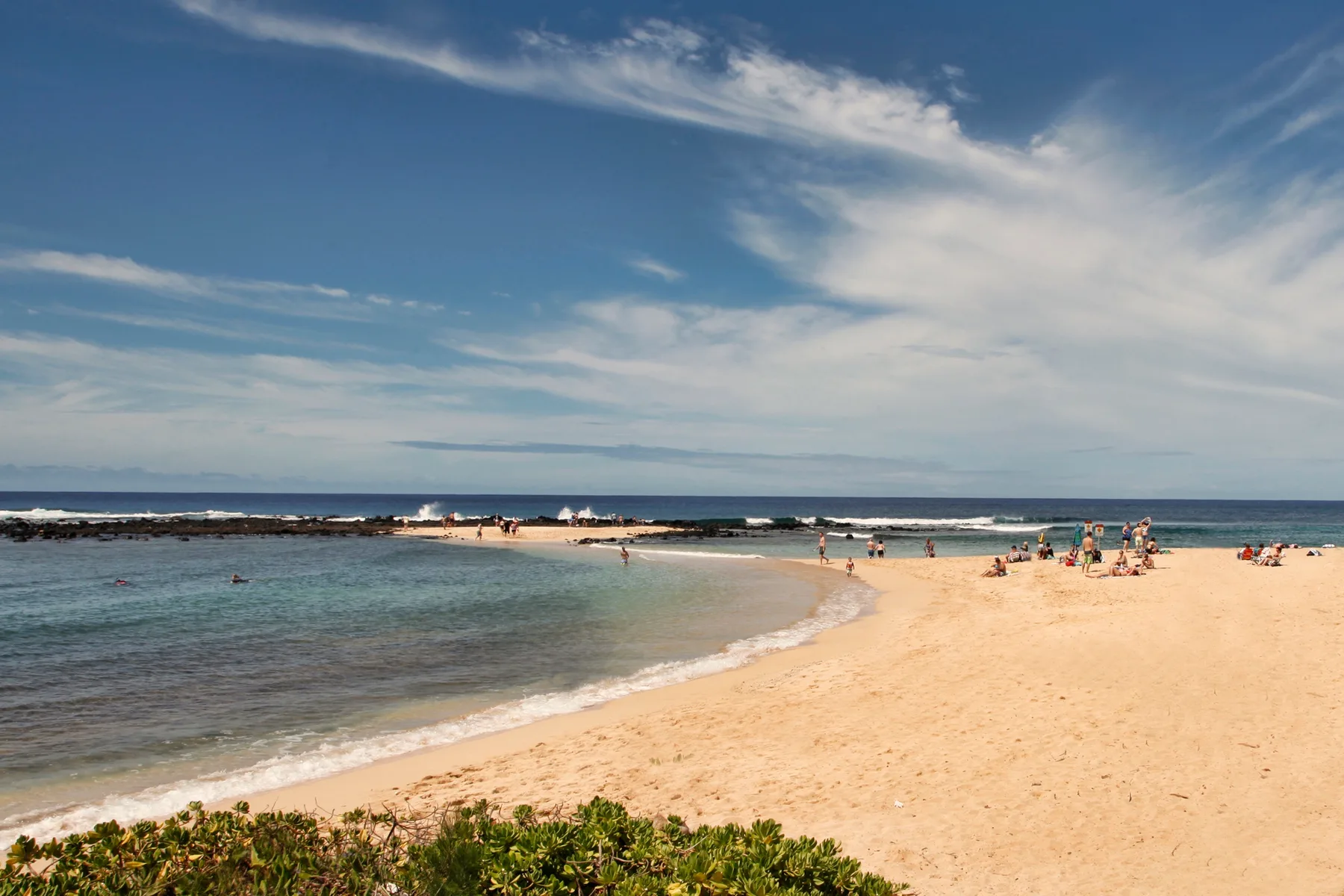 A sandy beach curves beside calm water beneath a partly cloudy sky.