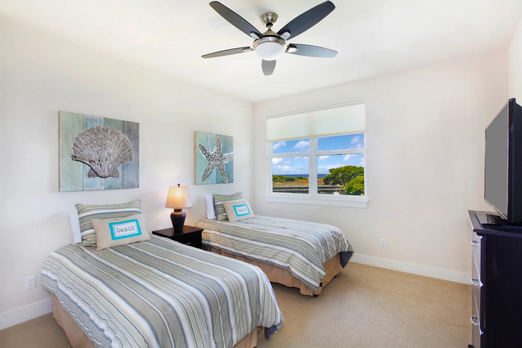 A bright bedroom with two beds and a window overlooking greenery.