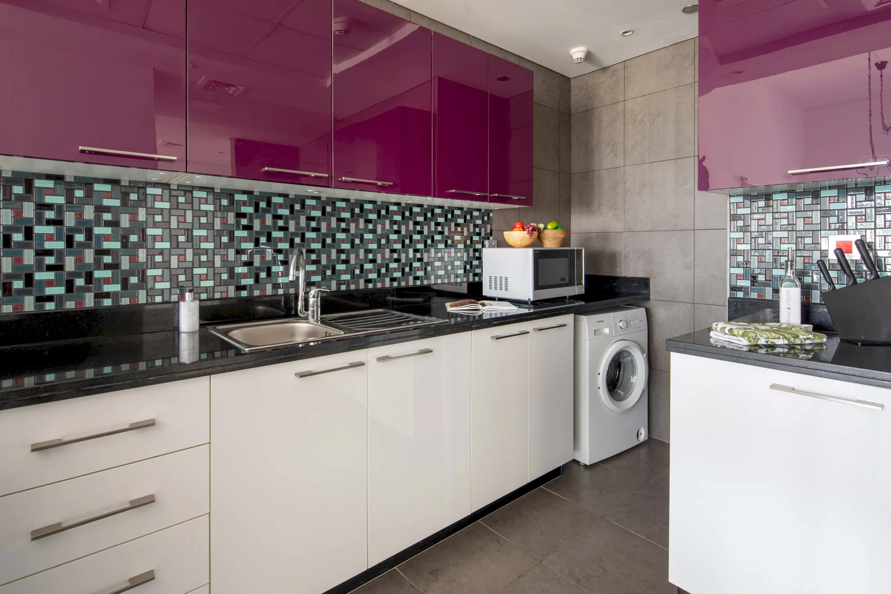 Una cocina moderna con gabinetes brillantes, un salpicadero de azulejos y una lavadora.