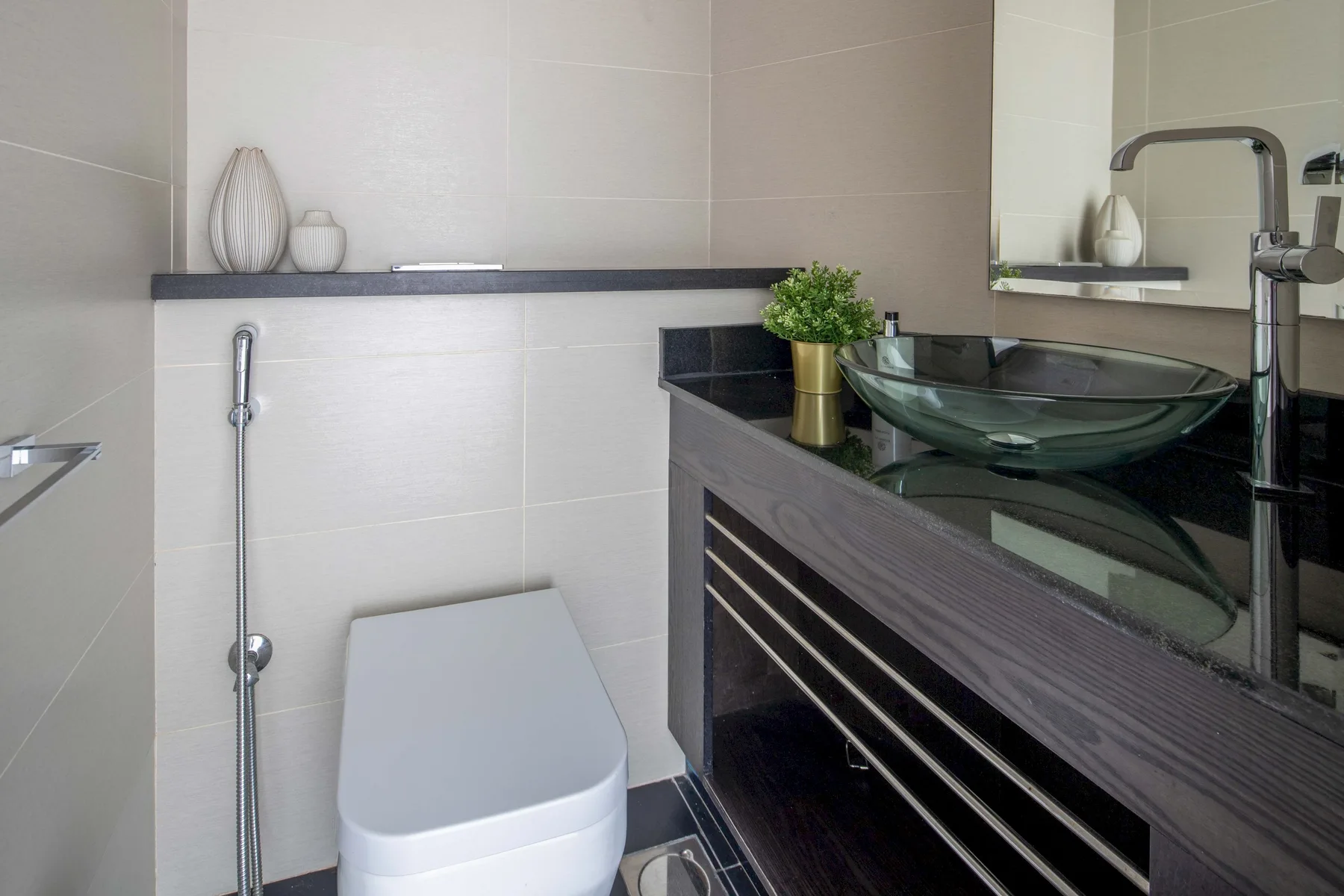 Un baño moderno con inodoro, mueble oscuro y lavabo de vidrio.